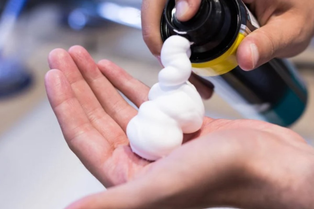 Persona spruzza sulla mano la schiuma da barba