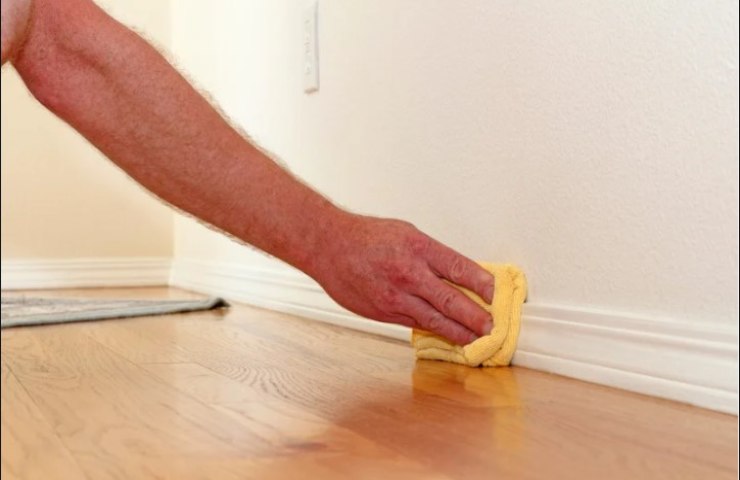 uomo pulisce con una pezza il battiscopa