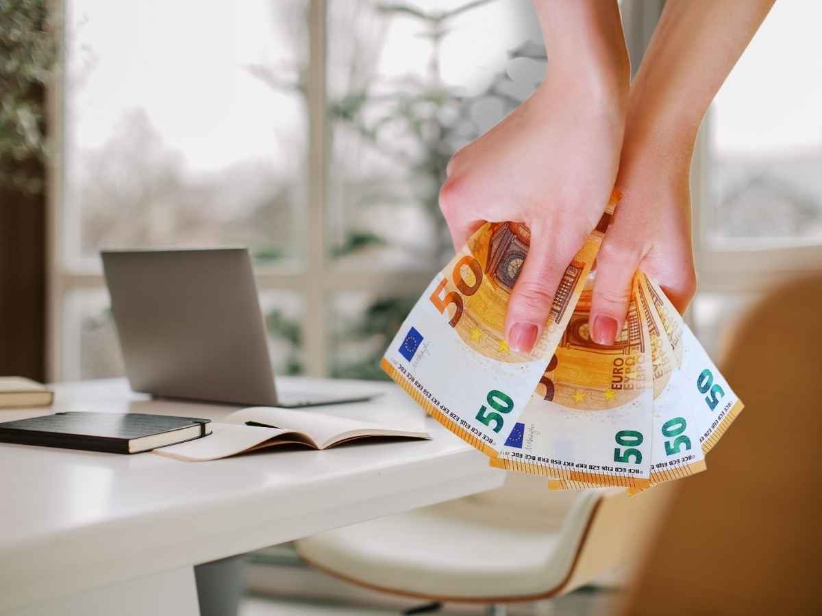 sfondo tavolo con pc in primo piano donna che tiene banconote tra le mani