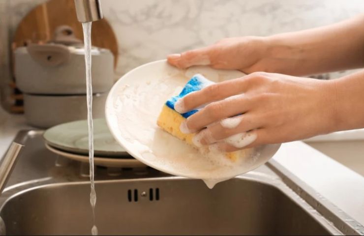 Persona lava i piatti con una spugnetta 