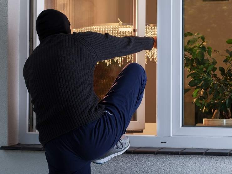 ladro che tenta di entrare in casa dalla finestra