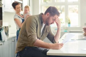 Uomo preoccupato osserva documenti con dietro mamma e bimbo che lo osservano