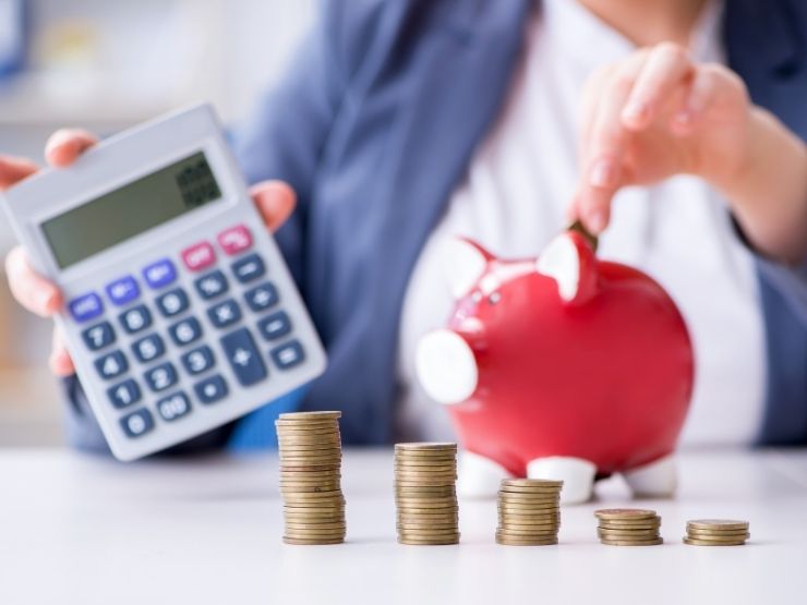 donna con in mano calcolatrice che mette monete nel salvadanaio