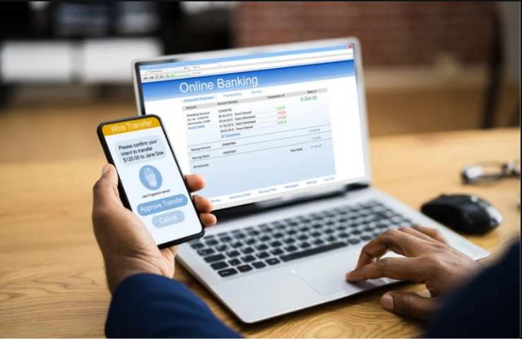 persona al pc controlla l'app della banca anche sul telefono 