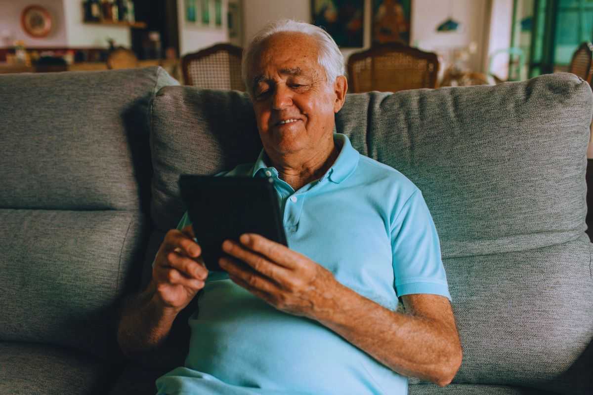 Anziano sorridente che usa tablet su divano