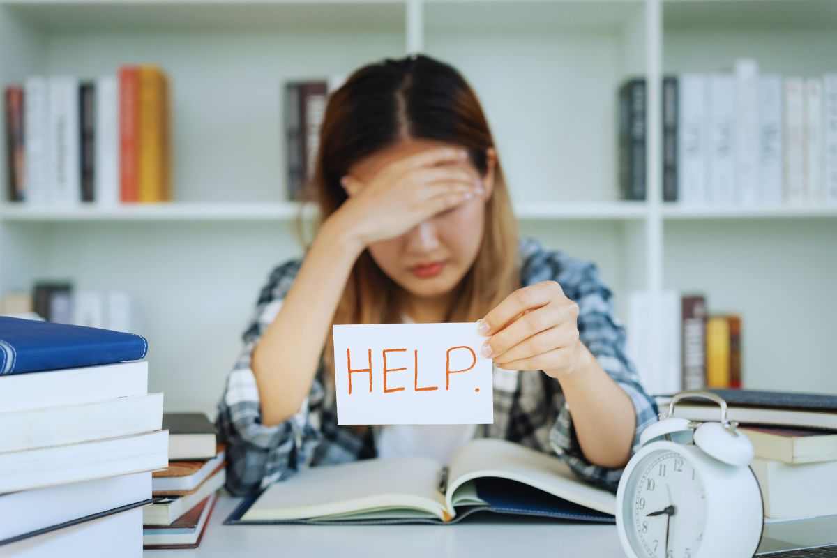 Ragazza che mostra il cartello "Help" mentre studia