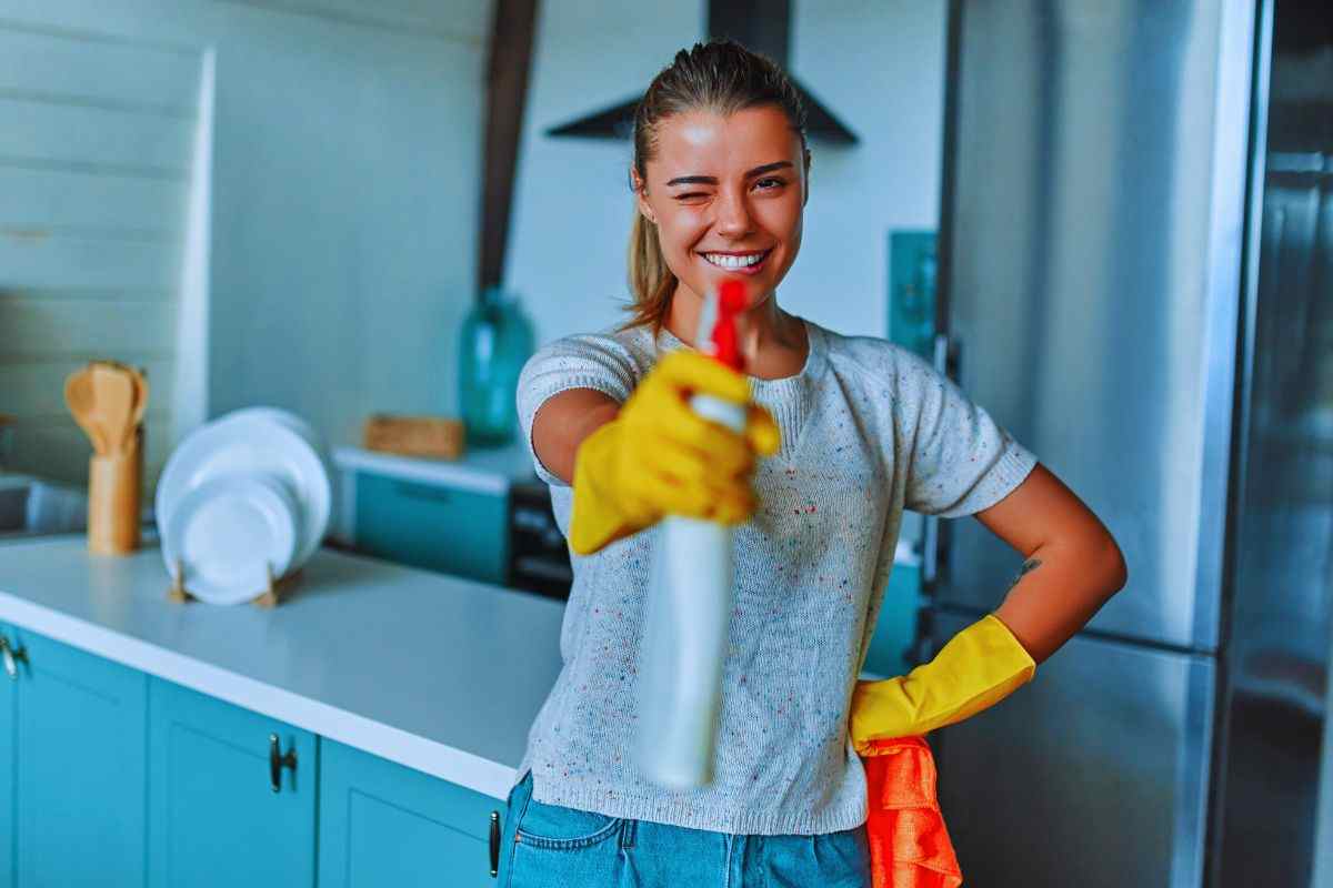 Ragazza con sgrassatore in mano che fa l'occhiolino e sorride