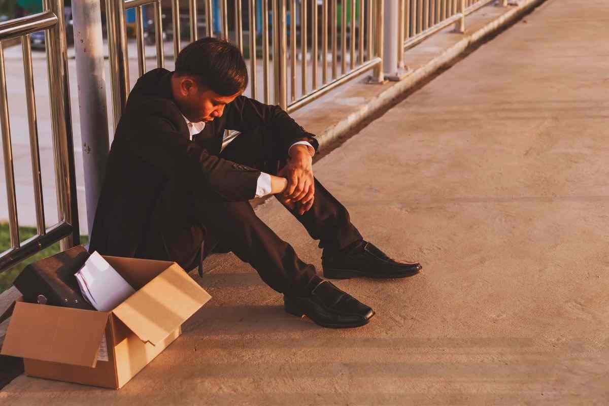 Uomo seduto in strada accanto a scatolone contenente effetti personali