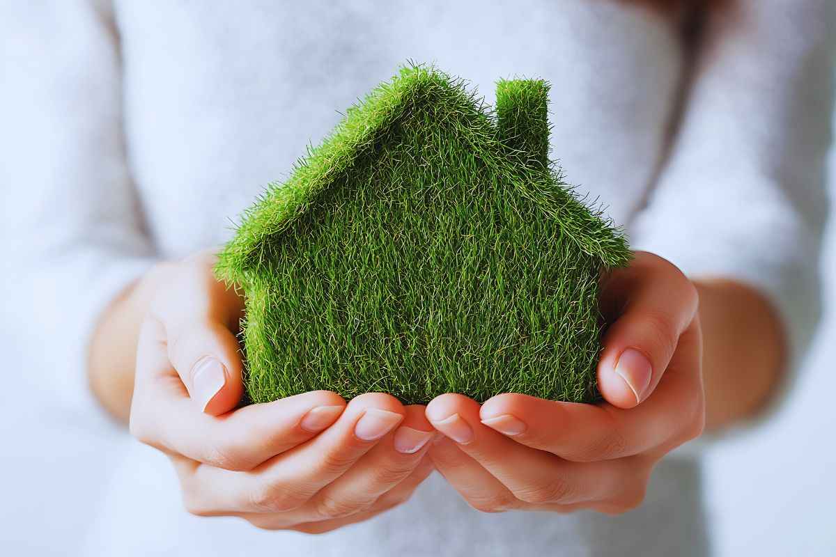 Donna che tiene in mano un modellino di casa fatto con l'erba