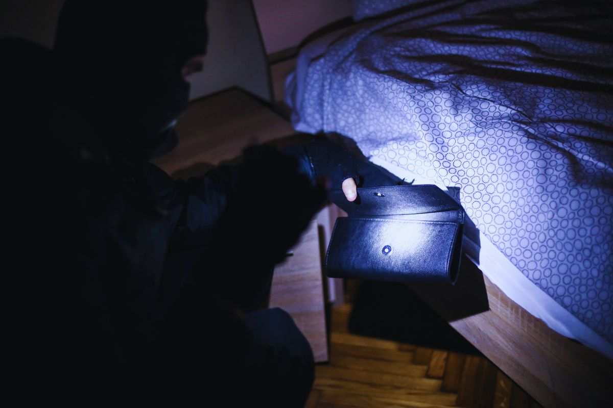 Ladro che svuota portafoglio accanto ad un letto