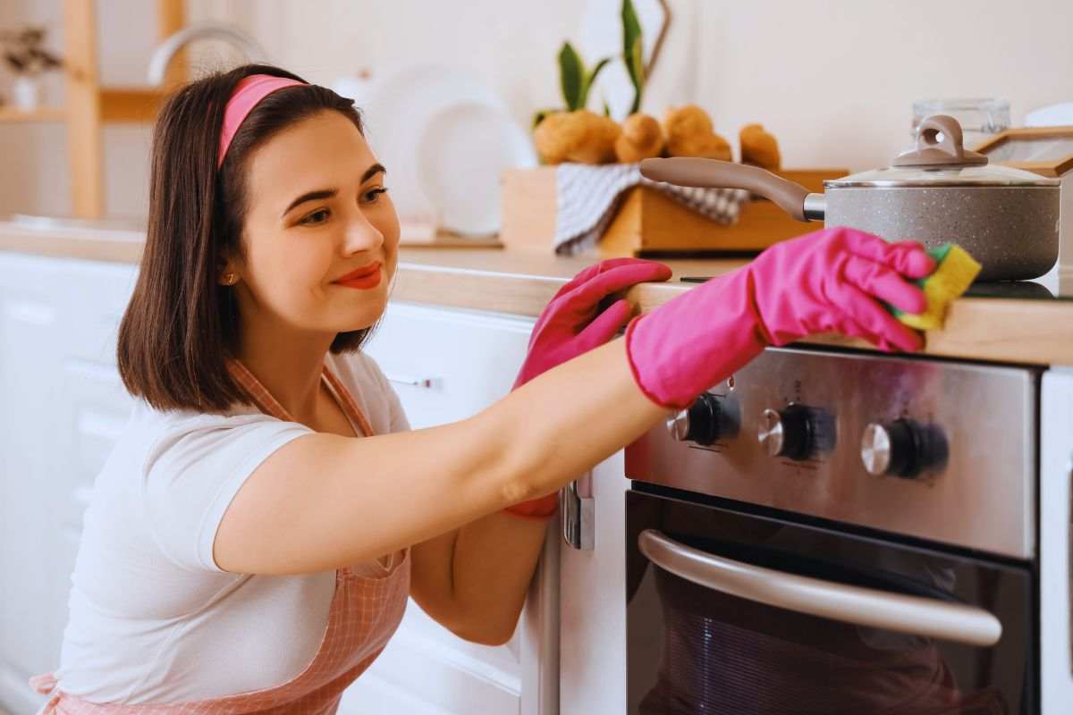Ragazza sorridente che pulisce forno e piano cottura