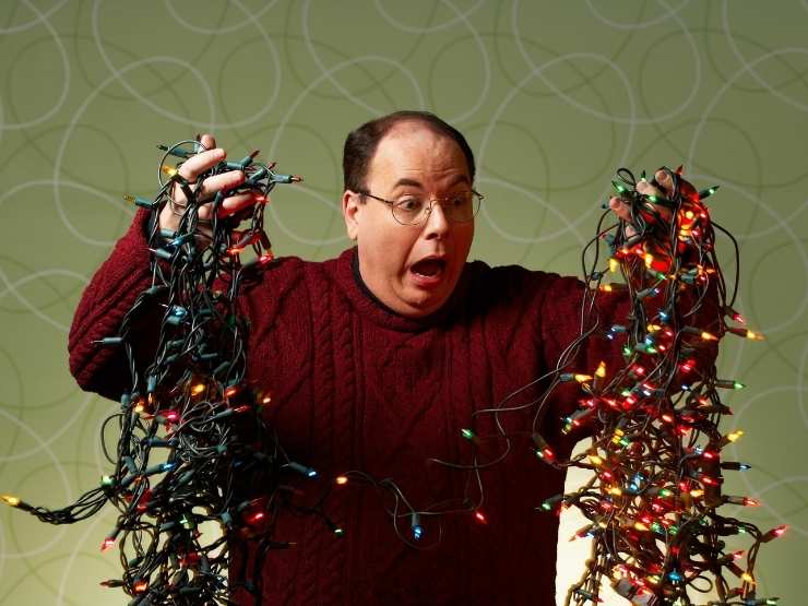 uomo con espressione sgomenta che tiene in mano luci natalizie