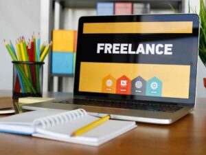 pc acceso, sullo schermo scritta freelance e taccuino sul tavolo