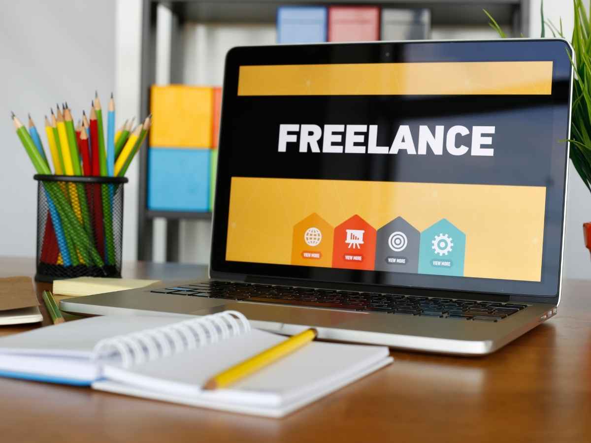 pc acceso, sullo schermo scritta freelance e taccuino sul tavolo