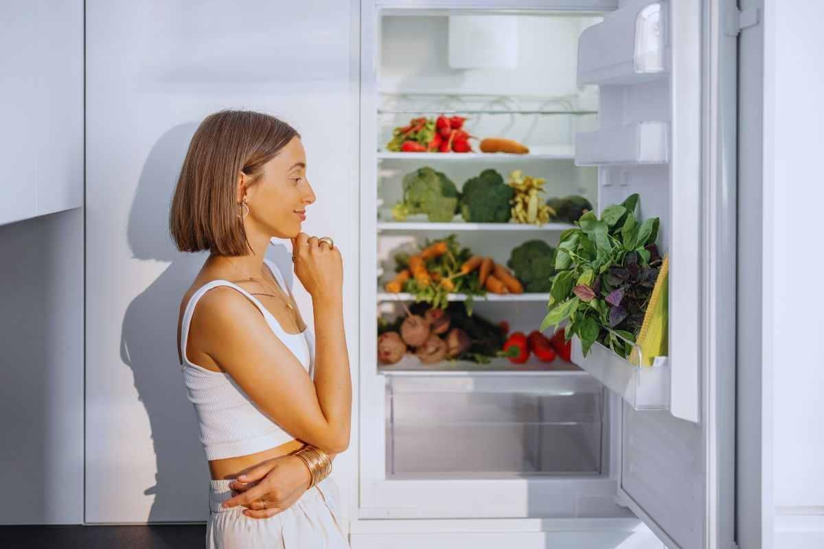 Ragazza che guarda gli scaffali di un frigorifero pieno di ortaggi