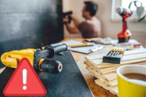 Operaio che fissa al muro un pannello con il trapano e attrezzi da lavoro poggiati su un tavolo