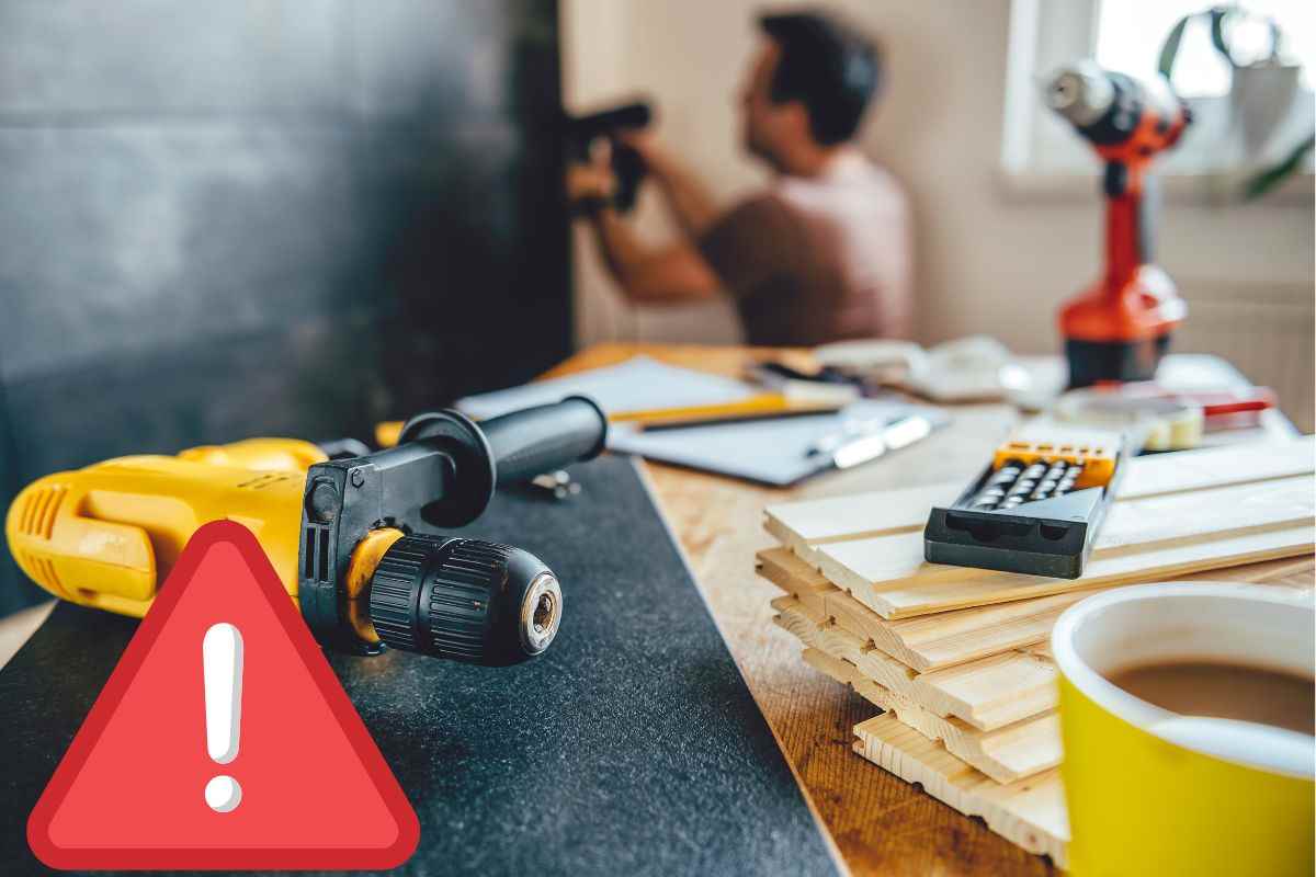 Operaio che fissa al muro un pannello con il trapano e attrezzi da lavoro poggiati su un tavolo