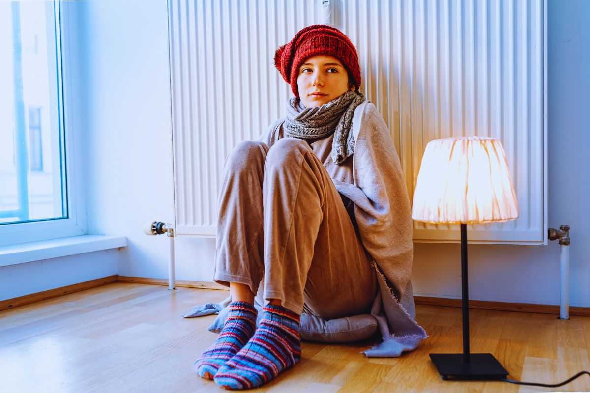 Ragazza infreddolita poggiata su termosifone
