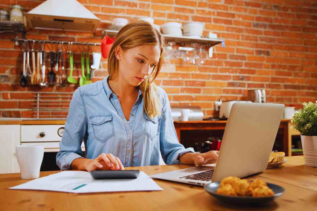 Donna seduta al tavolo della cucina che utilizza PC e calcolatrice