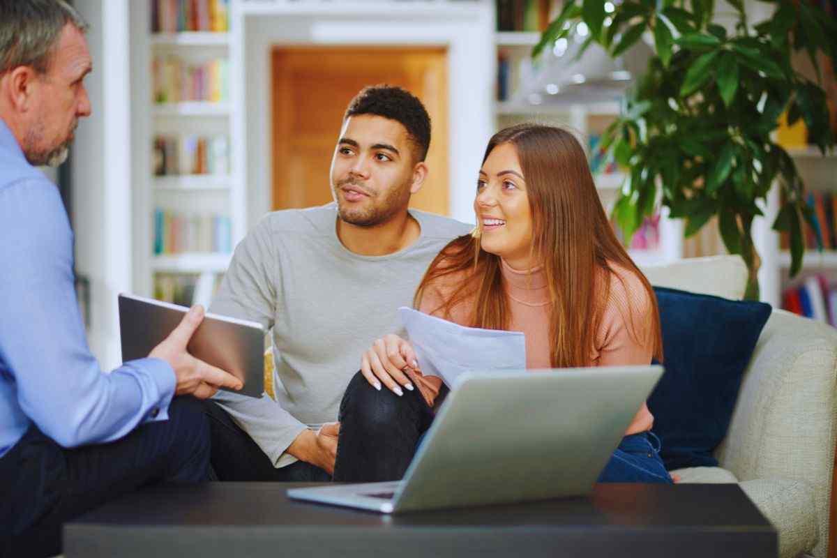 Giovane coppia che parla con un consulente finanziario che mostra loro i dettagli da un tablet