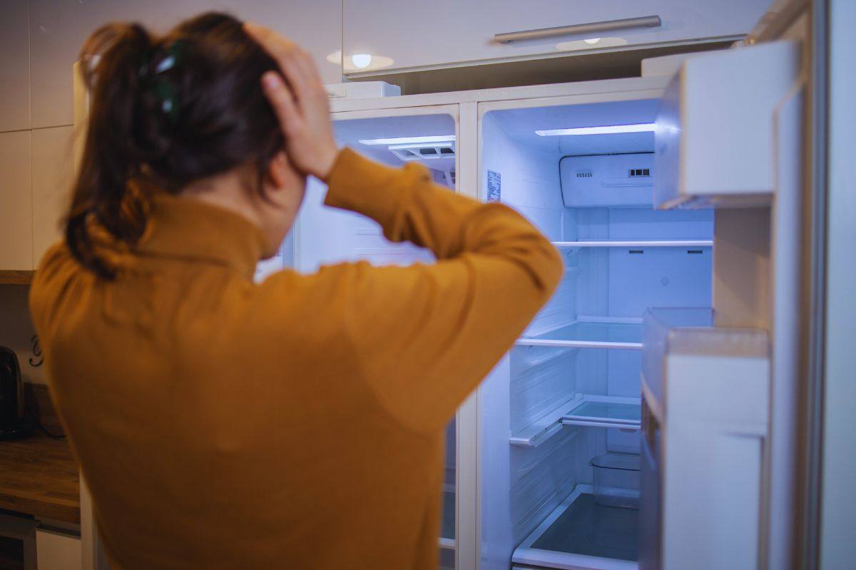 Donna che guarda il frigo vuoto e si mette le mani tra i capelli per la disperazione