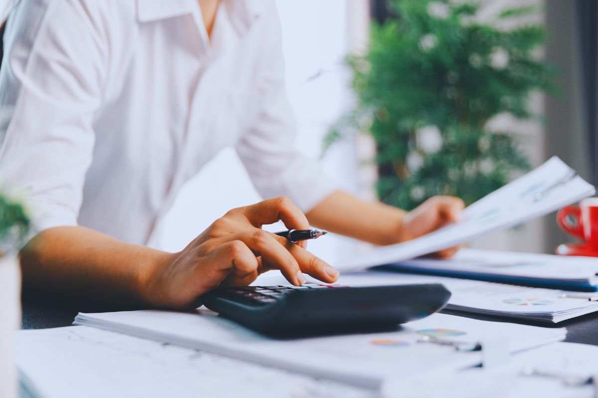 Persona che utilizza calcolatrice e scrivania piena di documenti