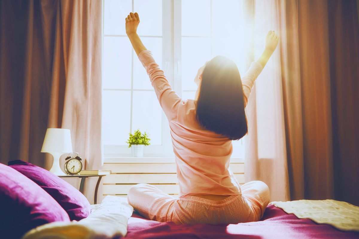 Donna che fa stretching a letto davanti alla finestra