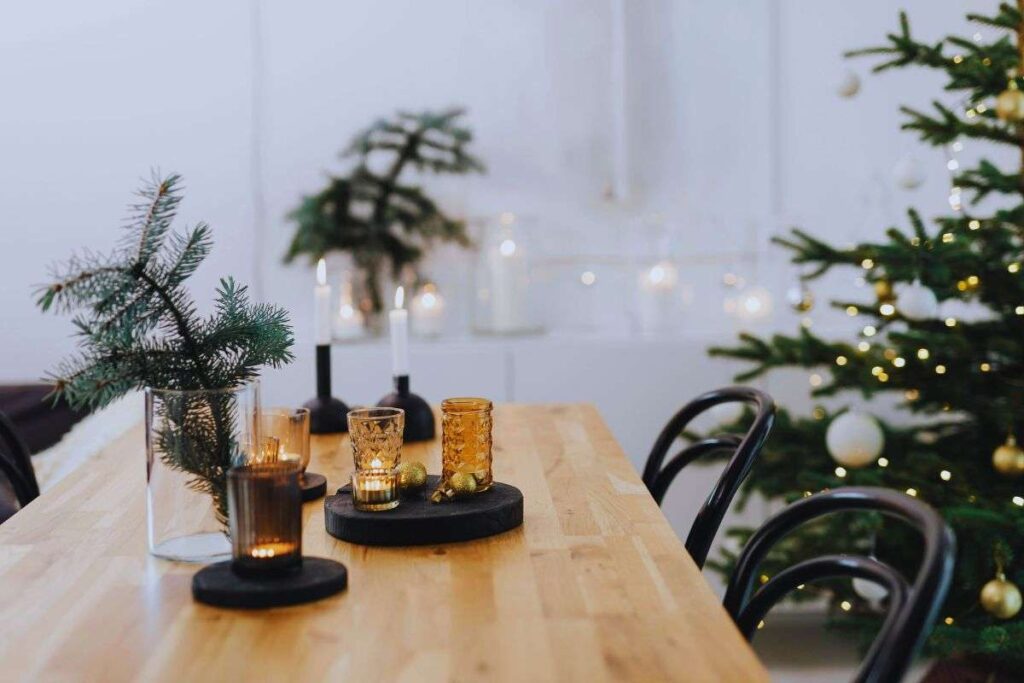 Tavolo in legno con sora bottiglie e bicchieri accanto ad un albero di natale con le luminarie accese