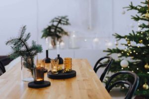 Tavolo in legno con sora bottiglie e bicchieri accanto ad un albero di natale con le luminarie accese