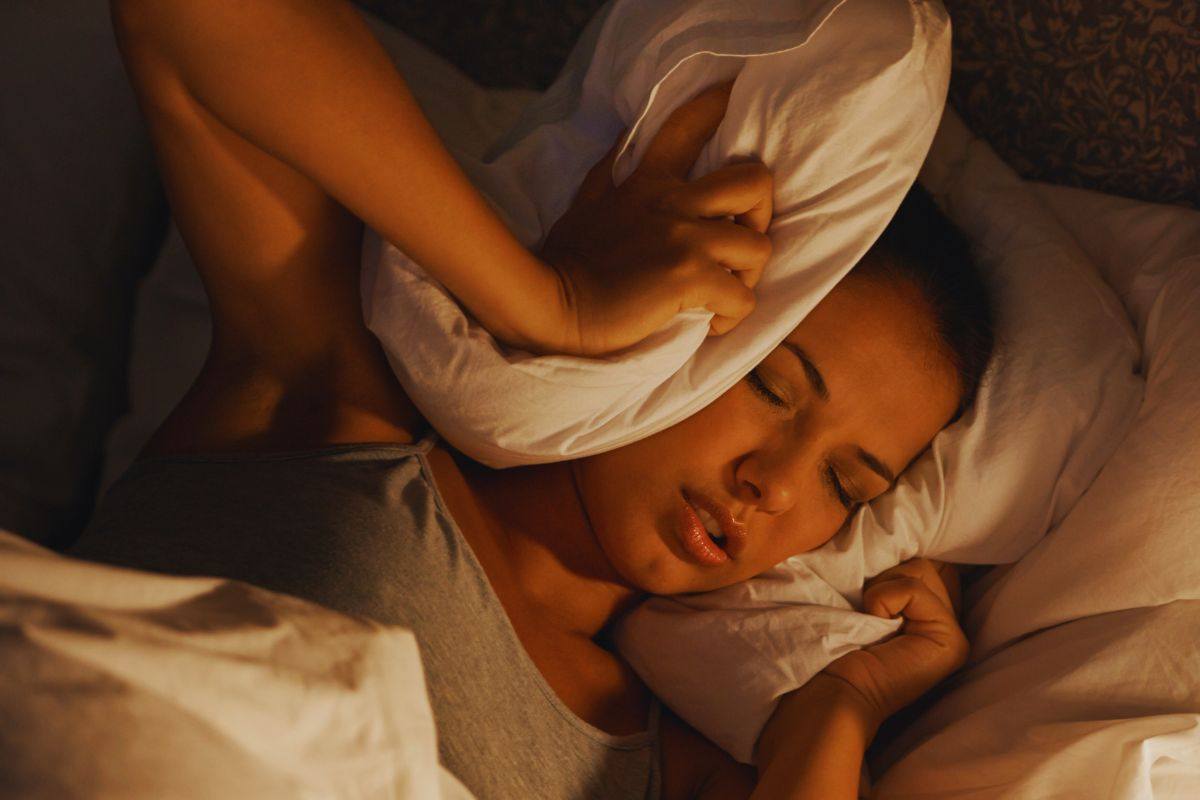 Ragazza che si tappa le orecchie con il cuscino mentre cerca di addormentarsi