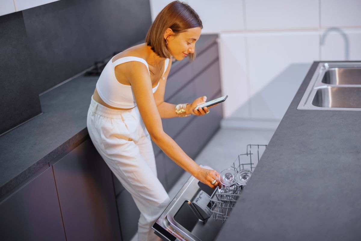 Ragazza che apre lavastoviglie mentre guarda lo smartphone