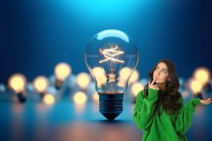 Ragazza pensierosa accanto a lampadina gigante e tante lampadine accese dietro