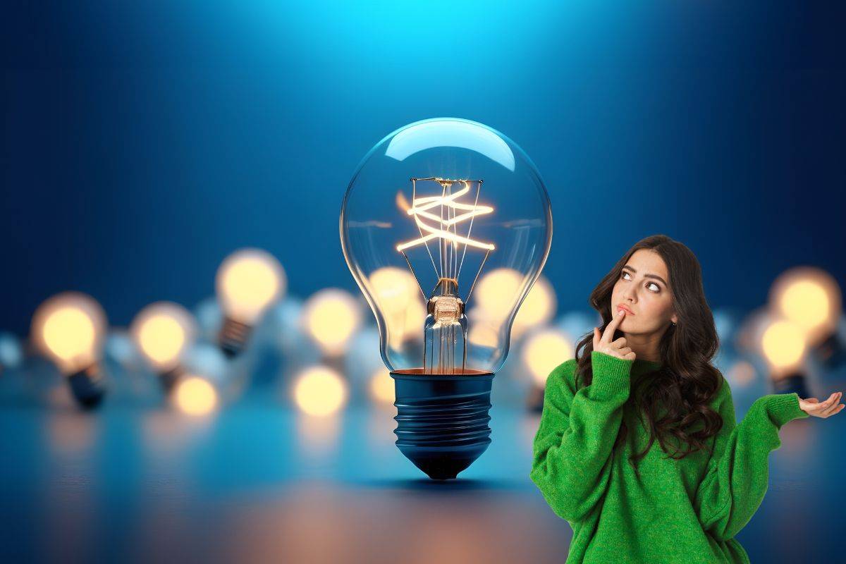 Ragazza pensierosa accanto a lampadina gigante e tante lampadine accese dietro