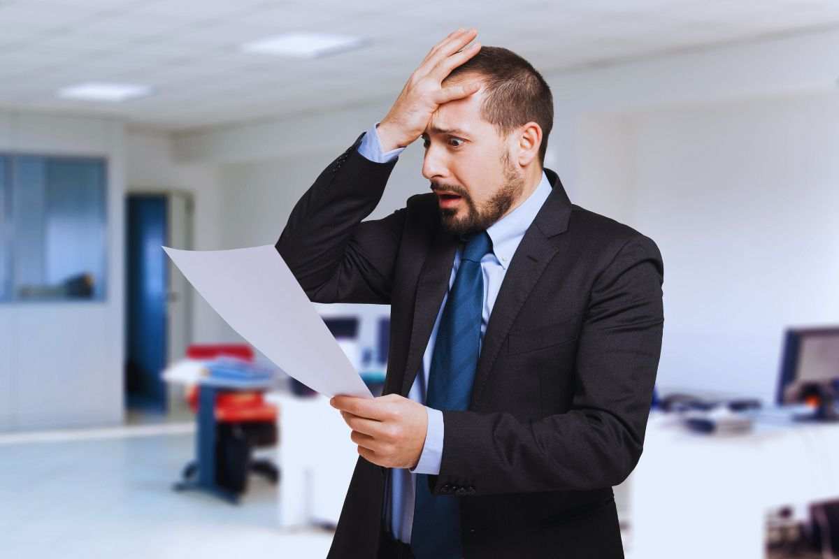 Uomo in abiti eleganti che si tiene la fronte in segno di disperazione mentre legge un documento