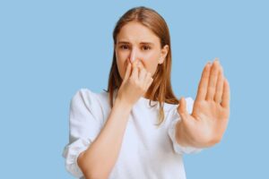 Ragazza con espressione disgustata che si tappa il naso con una mano e con l'altra fa il segno "Stop"