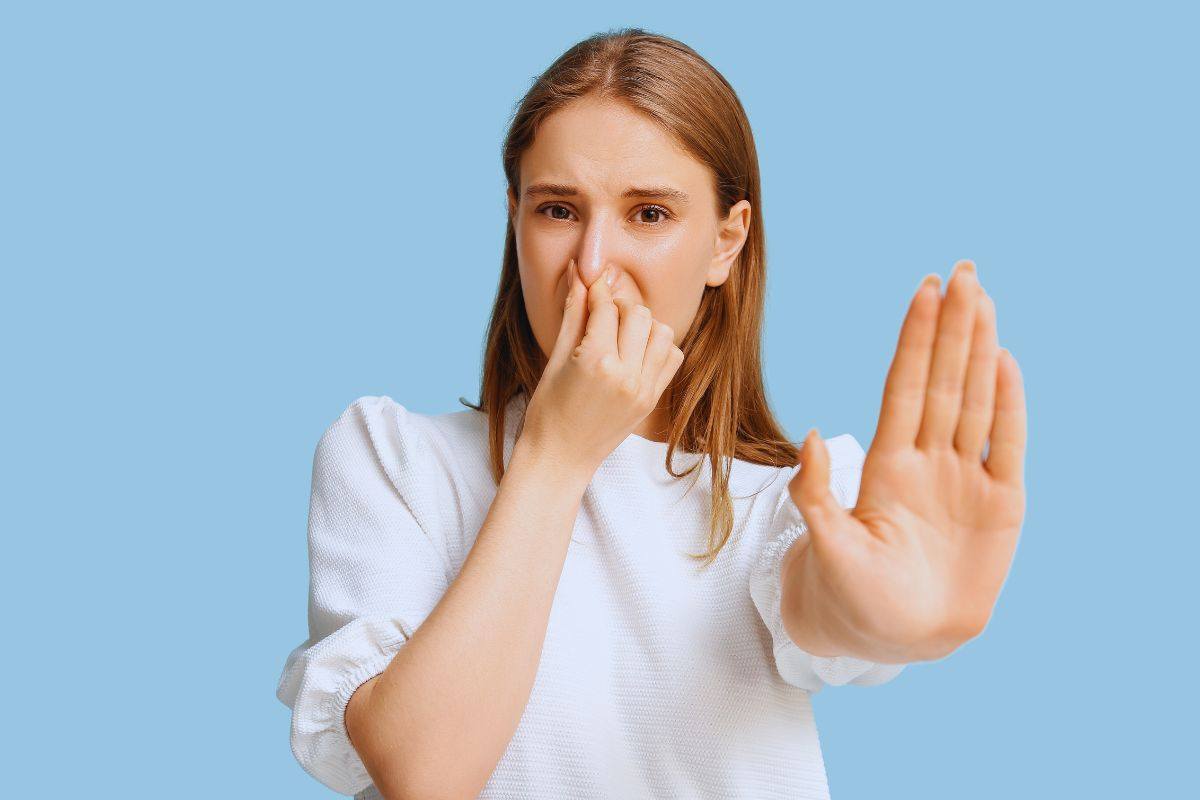 Ragazza con espressione disgustata che si tappa il naso con una mano e con l'altra fa il segno "Stop"