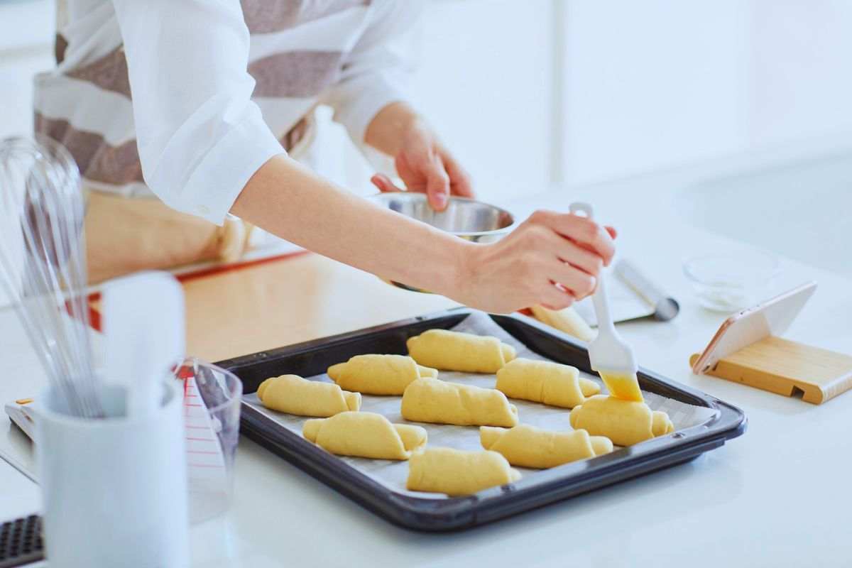 Donna che spennella forme di pane ancora crude poggiate su una teglia da forno