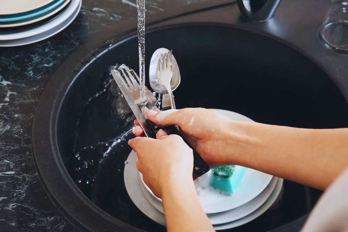 Donna che lava posate e piatti all'interno di un lavandino