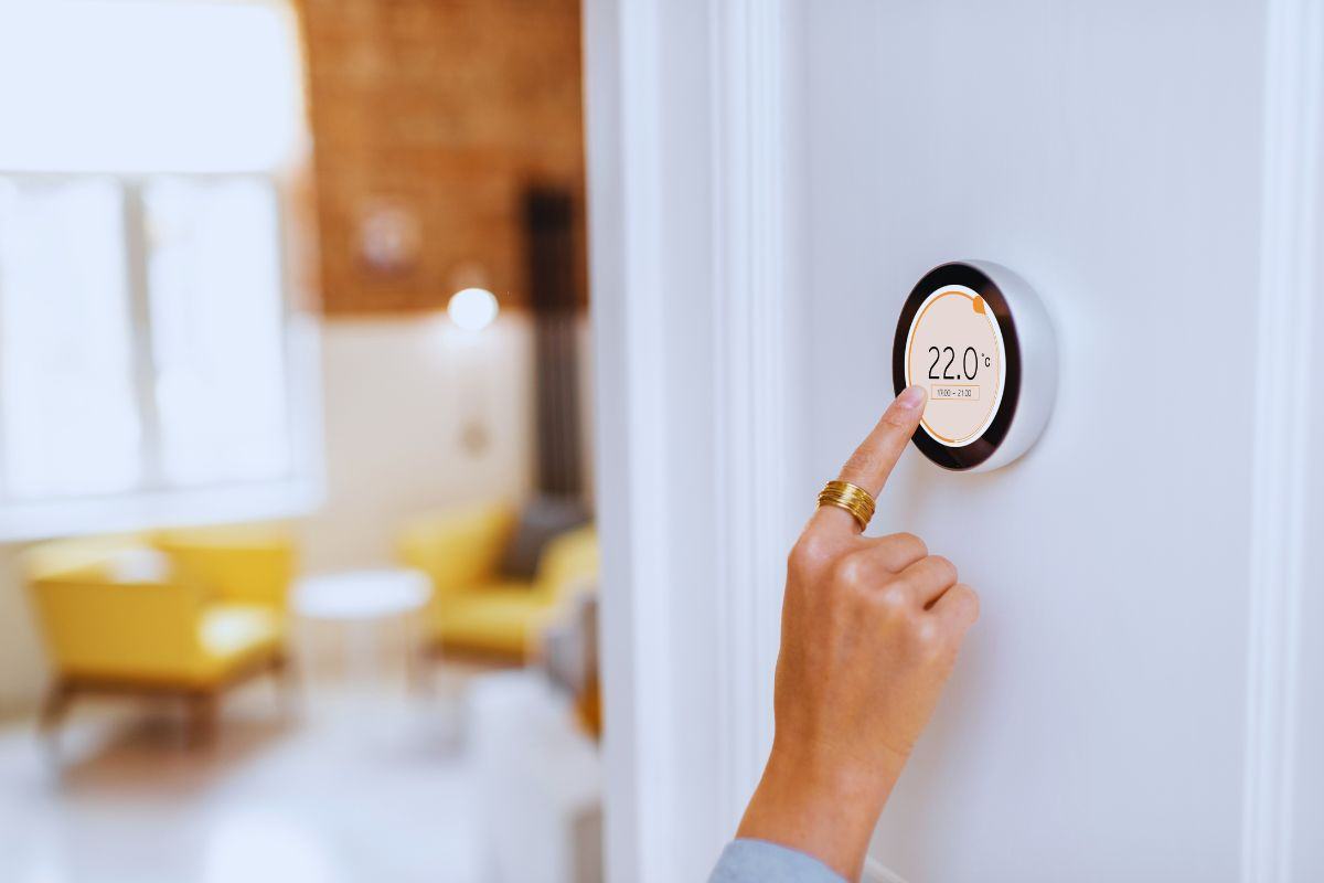 La mano di una donna che tocca il termostato digitale che si trova su una parete bianca