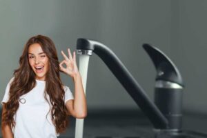 Ragazza che fa il gesto "Ok" e rubinetto d'acqua aperto