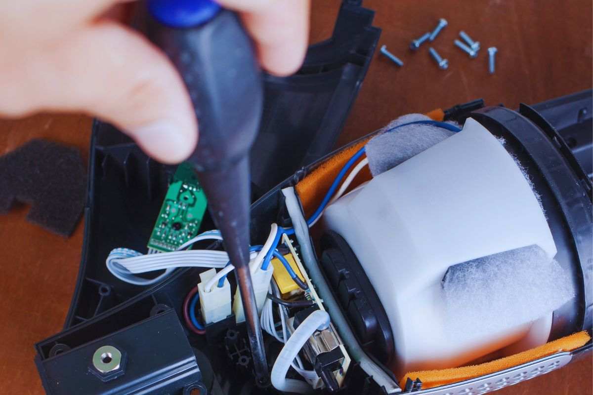 Aspirapolvere smontato e persona che utilizza il cacciavite per stringere una vite