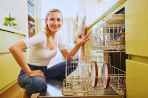 Donna sorridente accovacciata davanti ad una lavastoviglie aperta