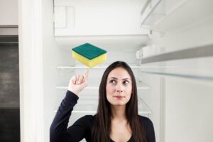 Giovane donna che indica una spugna per piatti che si trova all'interno di un frigorifero vuoto